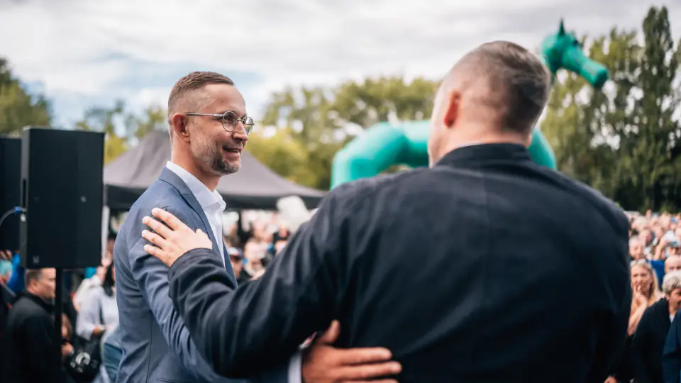 Daniel Wald begrüßt auf der Bühne einen Mann mit einer Umarmung, im Hintergrund das Publikum.